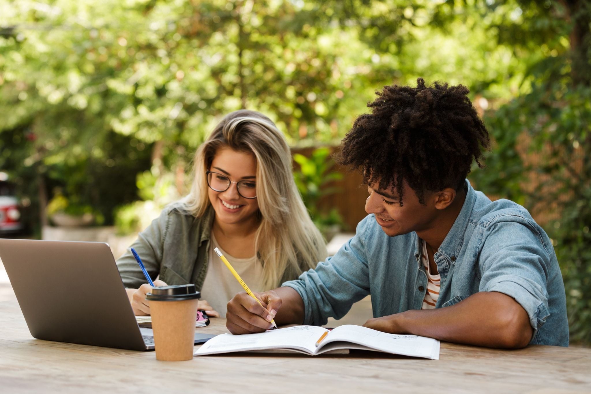 Two students studying outdoors with a laptop and notebooks.